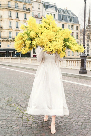 Late For Love is a photo of a girl in Paris in Ile St Louis with the biggest bunch of mimosa (wattles) and is part of a limited edition series named Young Girl in Bloom by photographer Carla Coulson celebrating women loving and believing in themselves and building their self esteem by trusting their intuition.