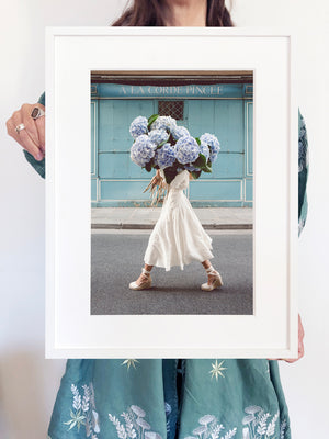 Out Of The Blue is a photo of a girl in Paris in St Germain des Prés holding the biggest bunch of baby blue hydrangeas and is part of a limited edition series named Young Girl in Bloom by photographer Carla Coulson celebrating women loving and believing in themselves and building their self esteem by trusting their intuition.