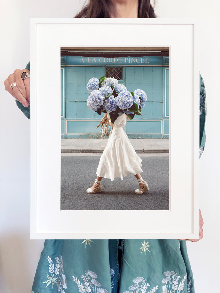 Out Of The Blue is a photo of a girl in Paris in St Germain des Prés holding the biggest bunch of baby blue hydrangeas and is part of a limited edition series named Young Girl in Bloom by photographer Carla Coulson celebrating women loving and believing in themselves and building their self esteem by trusting their intuition.